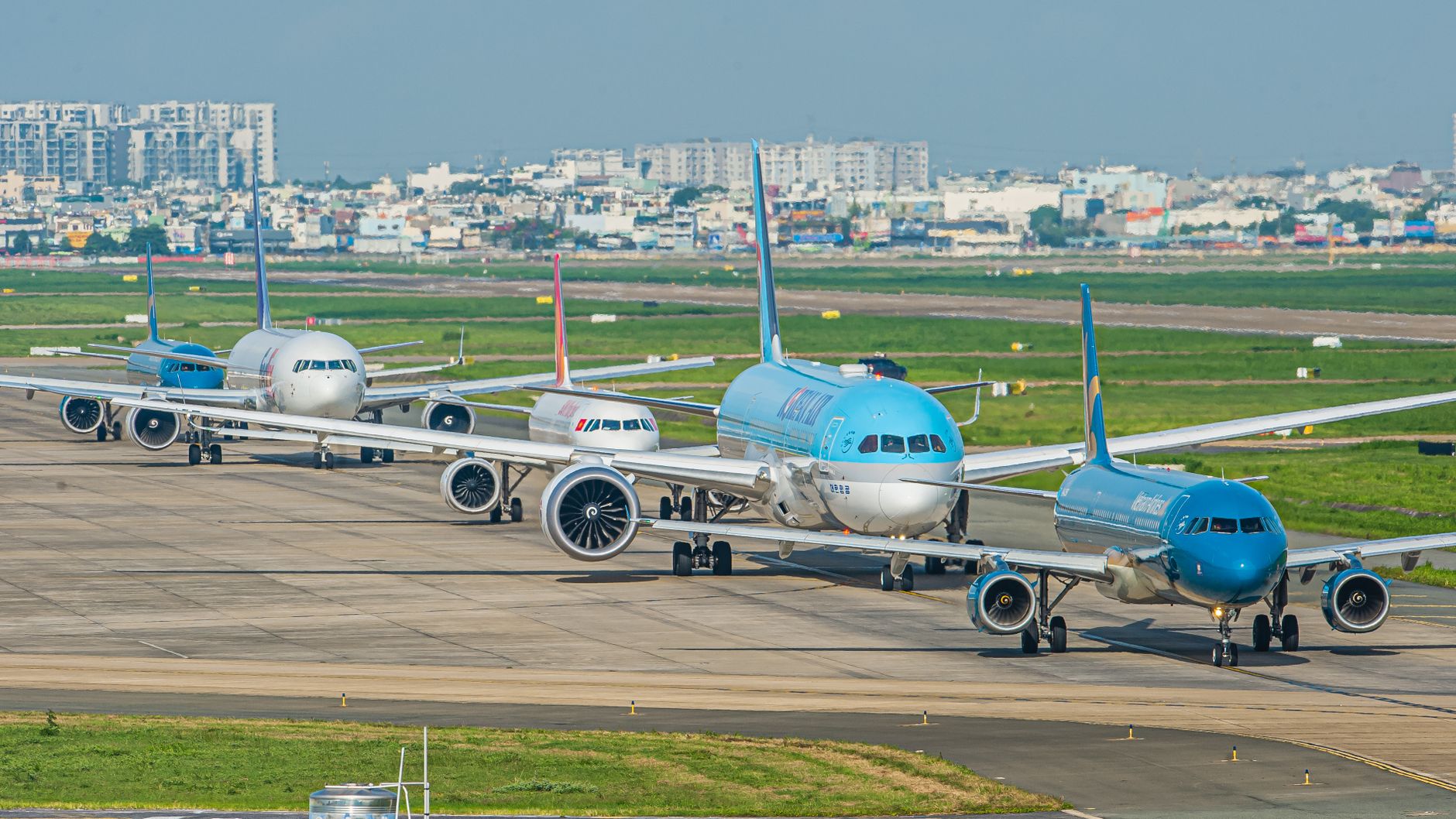 Multiple commercial aircraft parked at airport apron with city skyline and green fields beyond, depicting airport capacity and operations