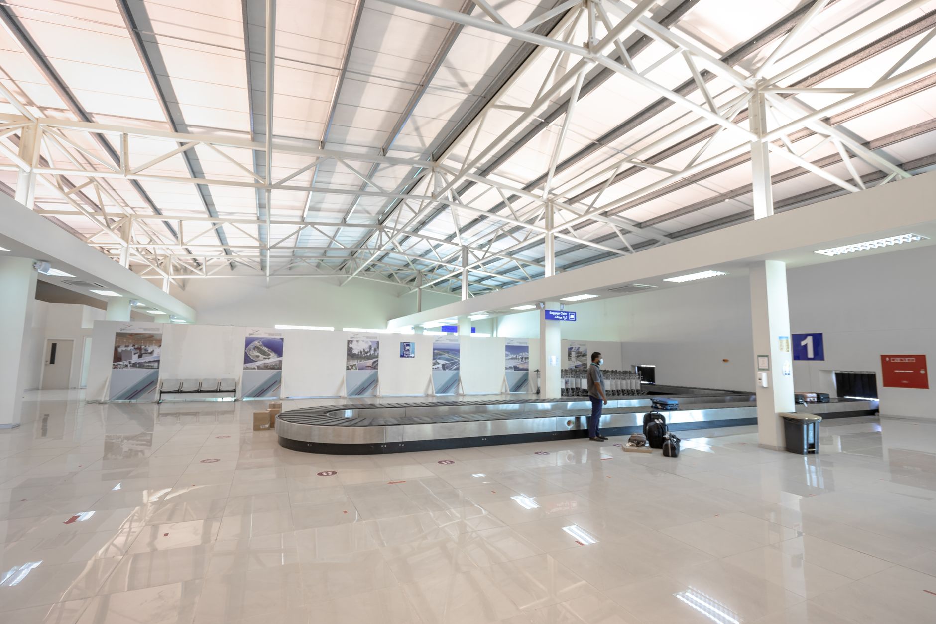 Modern airport baggage claim hall with carousel, skylights, and passenger with luggage