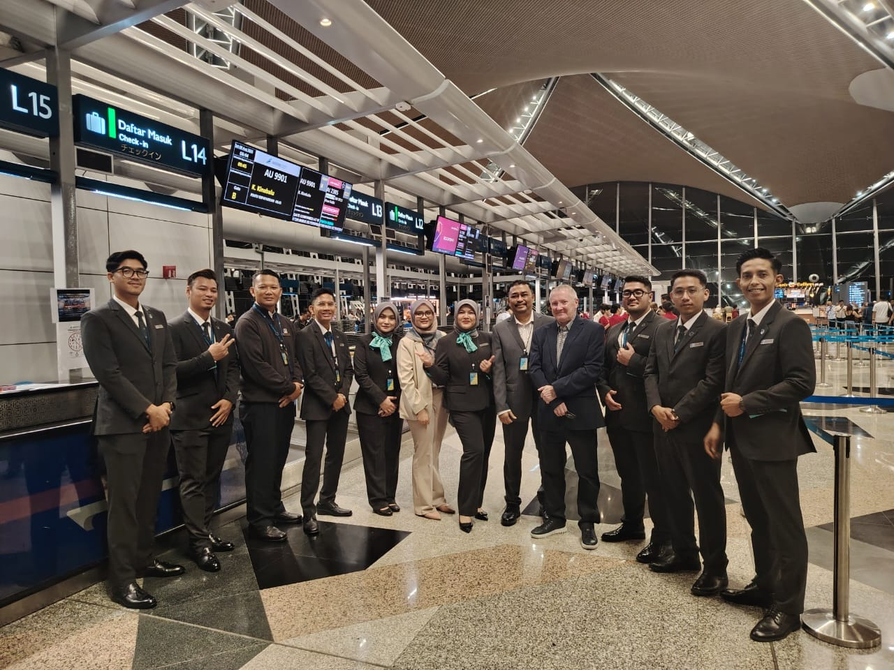 Uniformed airport staff team pose in modern terminal departure hall with gate signage and flight information displays
