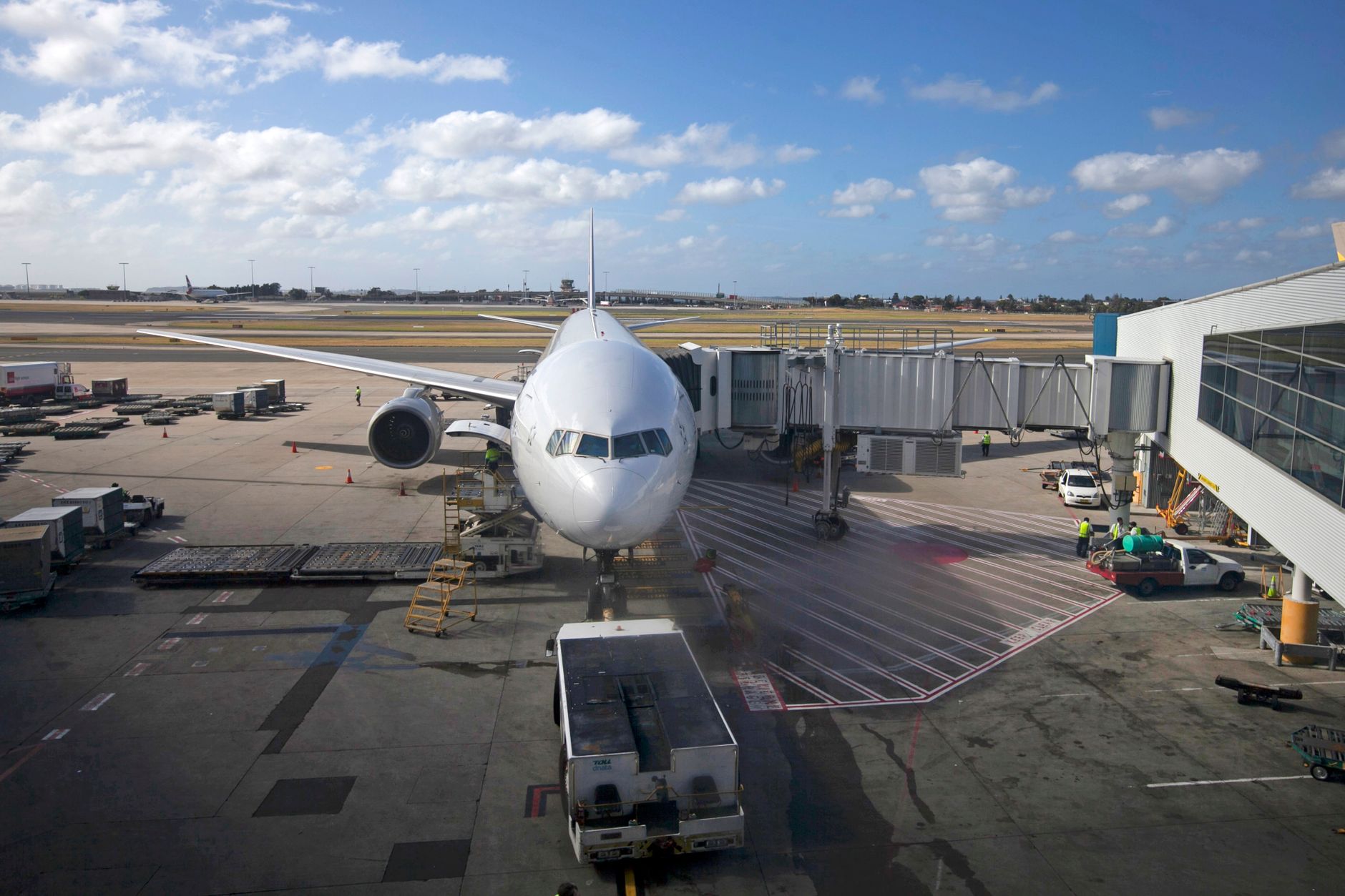 Wide-body aircraft docked at airport gate with ground support equipment and handling vehicles during daytime operations